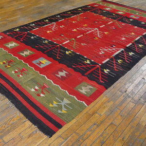 Geometric red, black, and green kilim rug displayed diagonally across distressed wooden flooring.