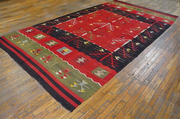 Geometric red, black, and green kilim rug displayed diagonally across distressed wooden flooring.
