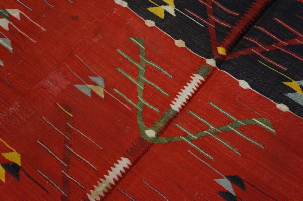 Flatweave rug close-up featuring stylized green, white, and red motifs on a deep red and dark navy background.