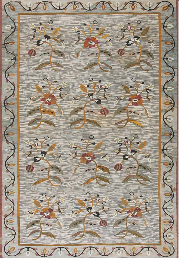 Light gray rug with wavy texture and rows of stylized floral motifs in gold, rust, and olive, framed by a complex scrolled border.