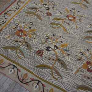 Flatweave rug with a striped gray background, large yellow and red florals, and a botanical border on wood planks.