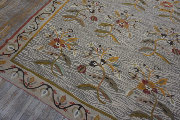 Flatweave rug with a striped gray background, large yellow and red florals, and a botanical border on wood planks.