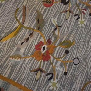 Flatweave rug detail showing stylized florals in red and orange against a gray and beige wavy striped field.