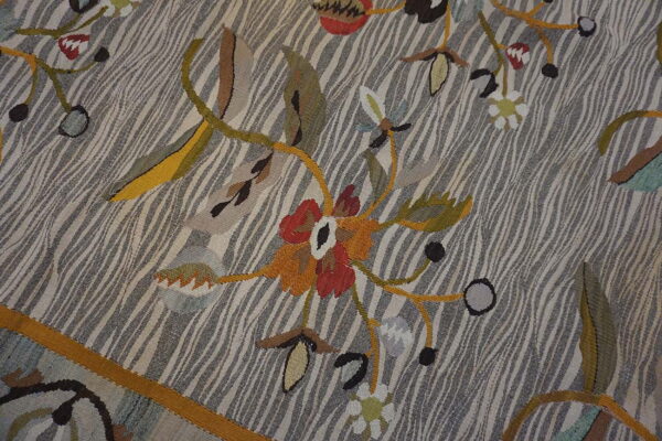 Flatweave rug detail showing stylized florals in red and orange against a gray and beige wavy striped field.