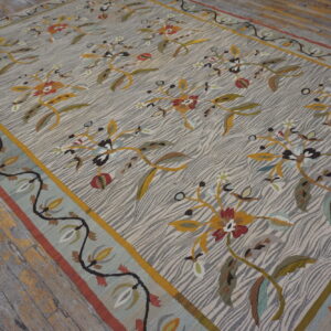 Colorful botanical patterns on a gray-striped rug with a blue border rests on worn, distressed wood flooring.