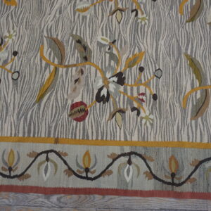 Flat-weave rug displaying mustard, red, and green botanical patterns over a striped grey and cream field.