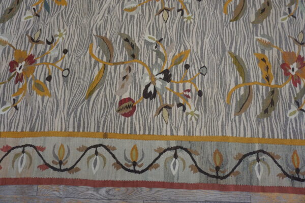 Flat-weave rug displaying mustard, red, and green botanical patterns over a striped grey and cream field.