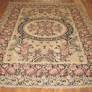 Large floral medallion rug in cream, pink, and navy colors resting on hardwood flooring.