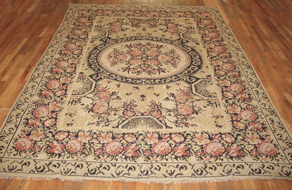 Large floral medallion rug in cream, pink, and navy colors resting on hardwood flooring.