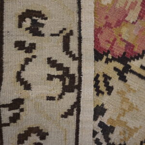 Flatweave rug detail featuring abstract borders in dark brown on beige, next to red and gold geometric patterns.