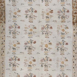 Off-white rug with repeating pastel floral vase patterns and complex geometric side borders in brown and cream.