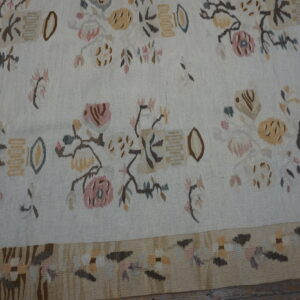 Low-pile cream rug with stylized floral and abstract motifs in pink, tan, brown, and blue on wood flooring.