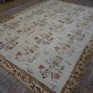 Cream flatweave rug featuring muted pink, yellow, and brown floral patterns and a wide patterned border on wood floors.