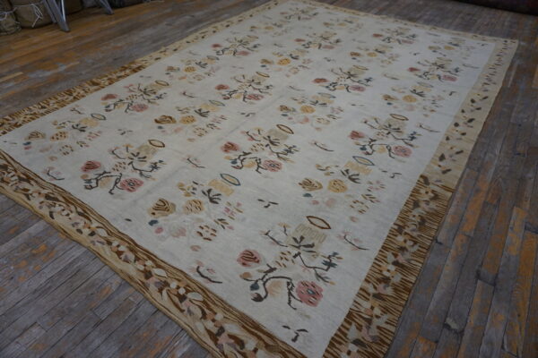 Cream flatweave rug featuring muted pink, yellow, and brown floral patterns and a wide patterned border on wood floors.