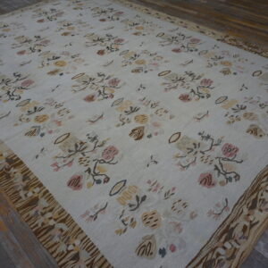 Flatwoven white rug displays scattered muted floral patterns and a wide, heavily patterned brown border on wood.