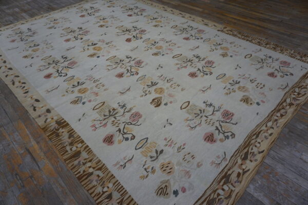 Flatwoven white rug displays scattered muted floral patterns and a wide, heavily patterned brown border on wood.