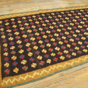 A dark flatweave rug with multicolored cross patterns and a wide gold zigzag border is placed on distressed wood floors.