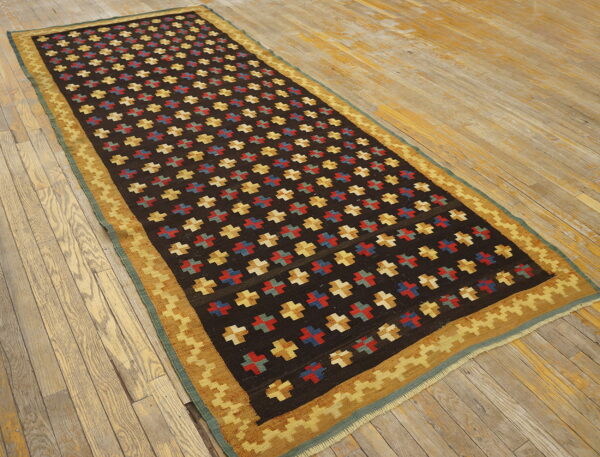 Dark runner rug featuring repeating red, blue, and yellow geometric cross patterns on distressed light wood floorboards.