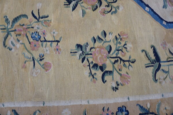 Pale yellow rug featuring scattered pink, navy, blue, and green floral vine motifs and a tan border.