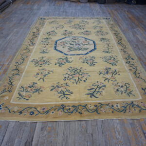 Pale yellow rug with blue and pink floral motifs and medallion on distressed gray hardwood floors.