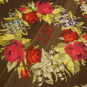 Dark brown rug featuring a bright floral wreath pattern with red Roman numerals centered among the red and pink roses.
