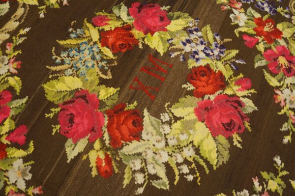 Dark brown rug featuring a bright floral wreath pattern with red roman numerals centered among the red and pink roses.