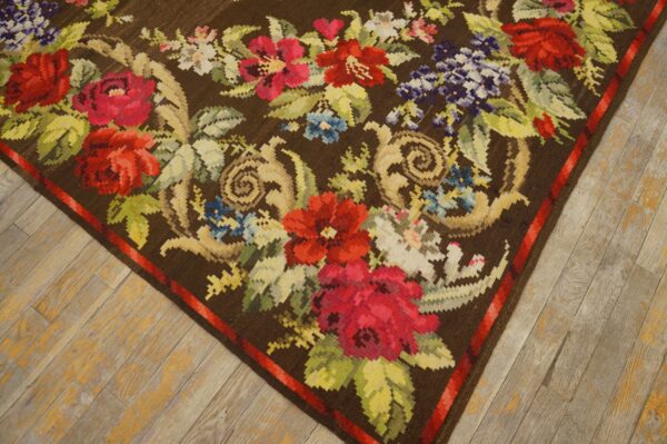 Flatweave dark brown rug featuring large red, pink, and blue flowers on distressed gray wood flooring.