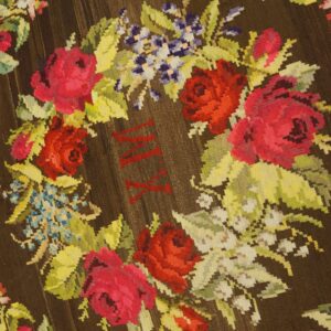 Brown flatweave rug with bright floral wreath design and visible red stitched Roman numerals in the center.
