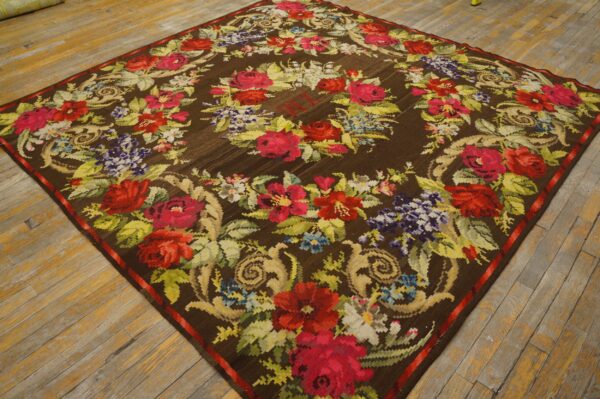 Floral flatweave rug with vibrant red and green motifs on a brown ground, displayed on worn wood flooring.