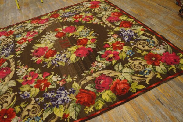 Brown rug with a dense floral wreath of red, pink, and purple flowers on aged wooden floors.