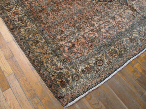 Muted pink and blue patterned area rug featuring a detailed border on light wood flooring.