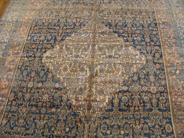 A traditional area rug featuring a navy blue field, intricate beige medallion, and detailed distressed patterns.