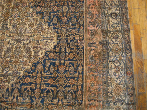 Detail of a traditional patterned rug in navy blue, beige, and terracotta against wood plank flooring.