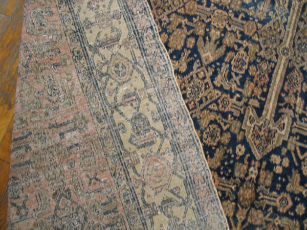 Two antique-style rugs overlap on a hardwood floor, one low-pile navy and gold, the other low-pile pink and beige.