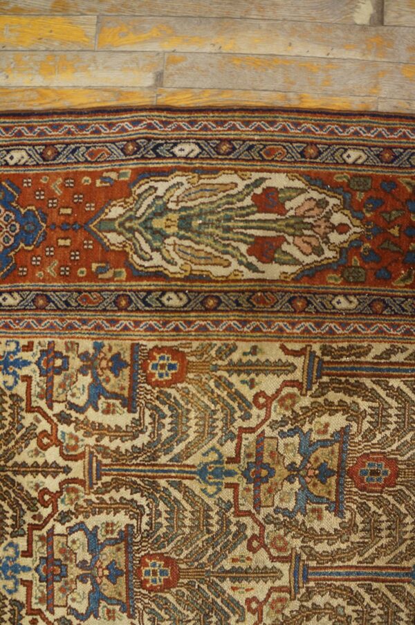 Ornate rug border in terracotta, blue, and cream sits on distressed yellow and gray wood planks.