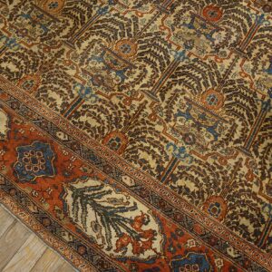 A low pile rug featuring intricate tan, brown, blue, and rust patterns rests on worn wooden floorboards.