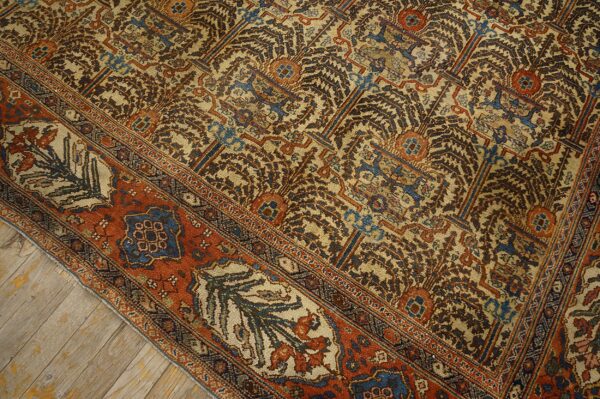 A low pile rug featuring intricate tan, brown, blue, and rust patterns rests on worn wooden floorboards.
