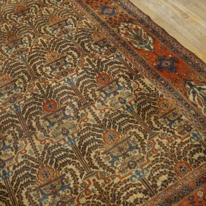 Detailed rug showing brown and blue stylized repeating motifs on a beige field with a rust border on wood flooring.