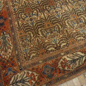 Intricate beige and brown tree-of-life rug with wide orange and blue geometric borders on wood flooring.