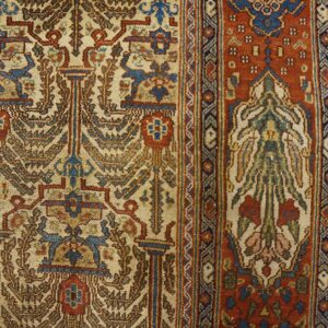 Detailed traditional rug featuring cream and blue motifs, a rust border, and visible knot texture on wood floor.