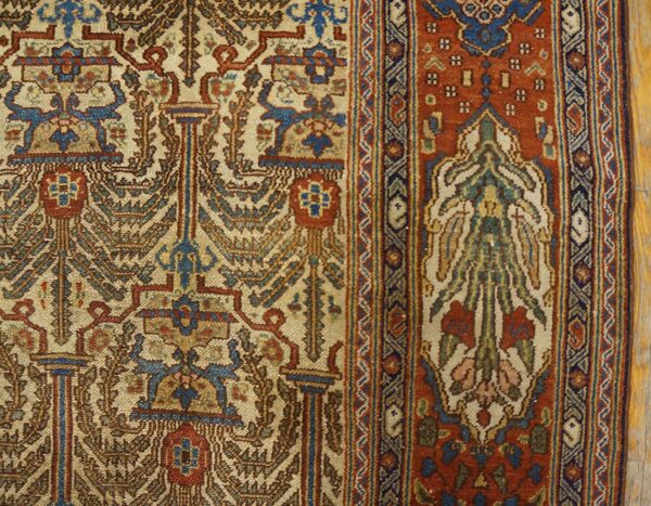 Detailed traditional rug featuring cream and blue motifs, a rust border, and visible knot texture on wood floor.