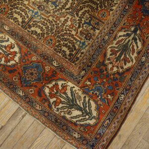 Corner detail of a traditional patterned rug in rust, cream, and indigo over worn diagonal wood floors.