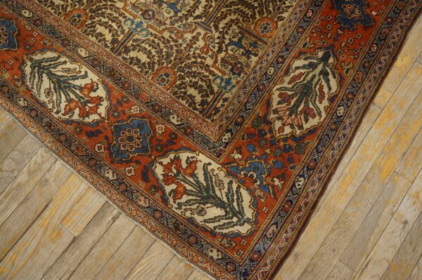 Corner detail of a traditional patterned rug in rust, cream, and indigo over worn diagonal wood floors.