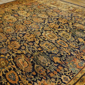 Navy rug with dense traditional gold, rust, and teal botanical patterns, displayed on wood floors.
