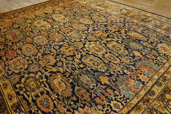 Navy rug with dense traditional gold, rust, and teal botanical patterns, displayed on wood floors.