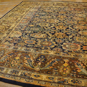 Dark blue ornamental rug with complex floral patterns and wide gold and brown borders on wood planks.