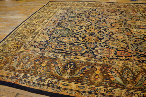 Dark blue ornamental rug with complex floral patterns and wide gold and brown borders on wood planks.