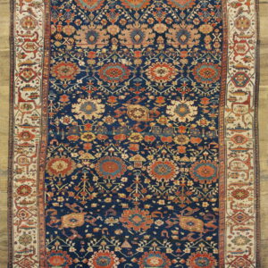 Deep navy rug with intricate rust and beige floral medallions, featuring a multi-colored geometric border on a tan background.