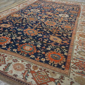 Ornate dark blue rug featuring rust-colored medallions and wide geometric light beige borders on wood flooring.