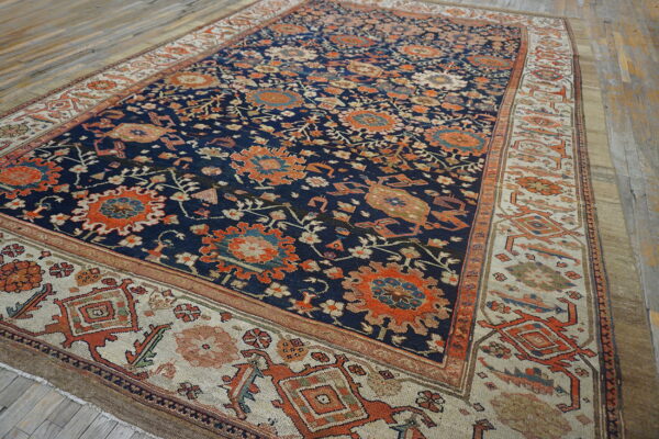 Ornate dark blue rug featuring rust-colored medallions and wide geometric light beige borders on wood flooring.